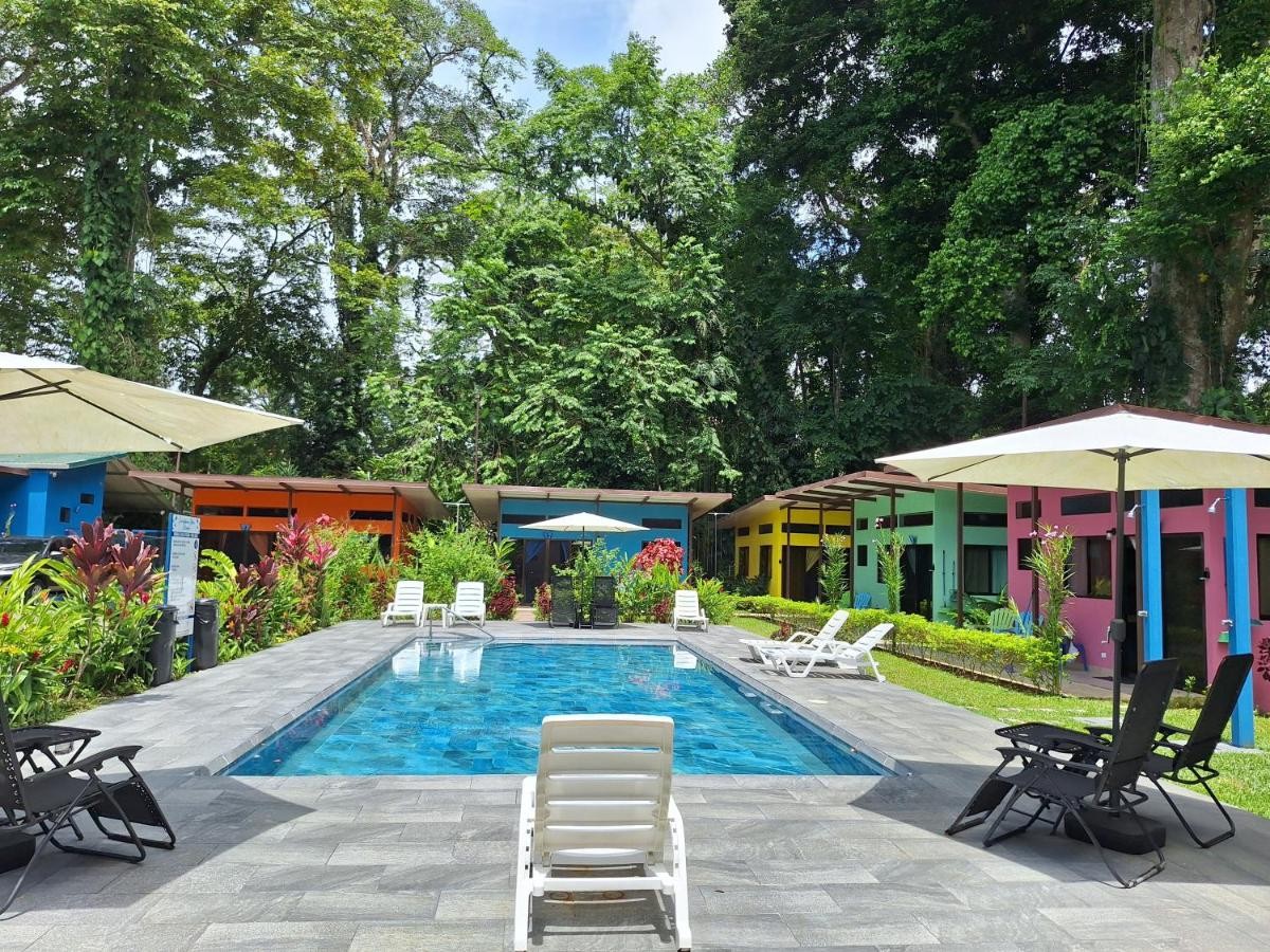 The pool at Caribbean Blue Morpho, ringed by orange, blue, yellow, green and pink casitas under jungle canopy.